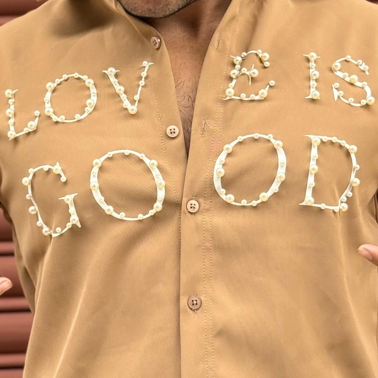 Person wearing a beige shirt with 'LOVE IS GOOD' text in front of a brown background