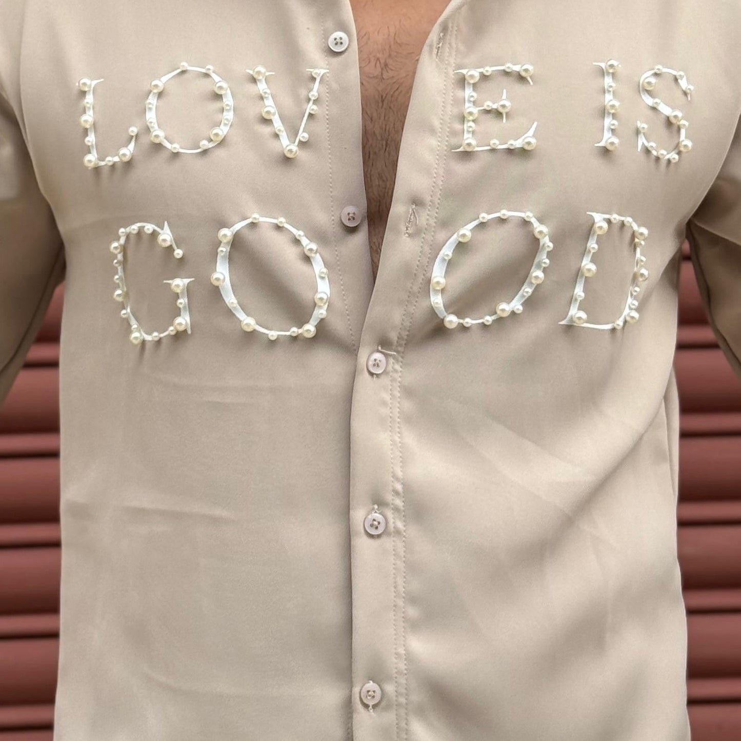 Person wearing a beige shirt with 'LOVE IS GOD' text in front of a brown background